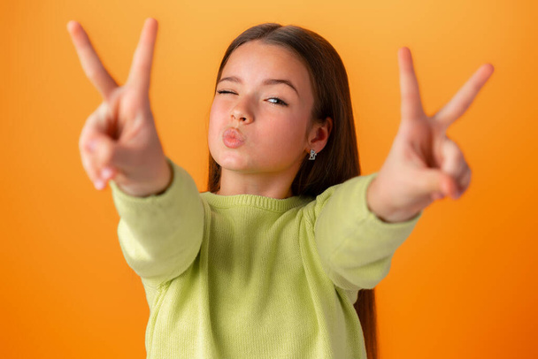 Teenager girl isolated on orange background showing victory sign - Foto, imagen