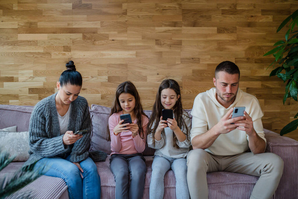 Family with two little daughters, everyone is using mobile phone in the living room. - Фото, зображення