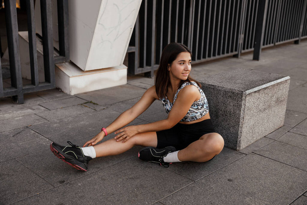 Adolescente sentada en el suelo y descansando después del entrenamiento de la ciudad el fondo - Foto, imagen