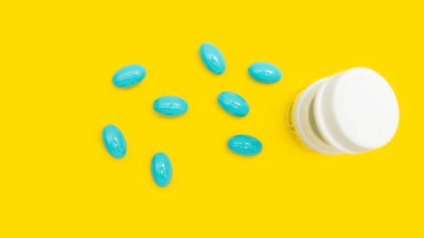 Pastillas o cápsulas azules para el tratamiento con frasco blanco sobre fondo amarillo, farmacia y concepto de medicina, vista superior. - Foto, Imagen