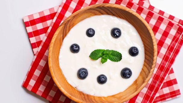 vista superior de los arándanos y la menta en tazón con yogur fresco aislado en blanco - Foto, Imagen