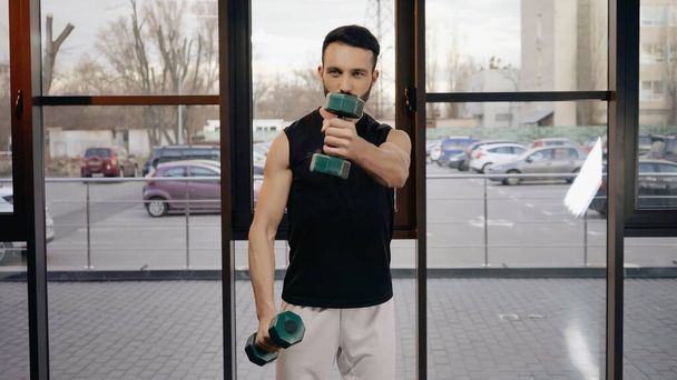 Sportsman holding dumbbells while training in gym  - Foto, Bild