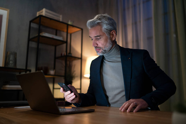 Mature businessman working on laptop at desk indoors in office at night. - Foto, Imagem