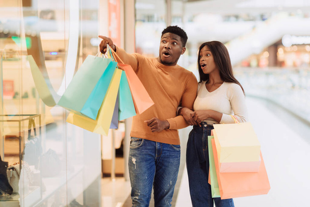 Excited black couple with shopping bags pointing at window - Photo, image