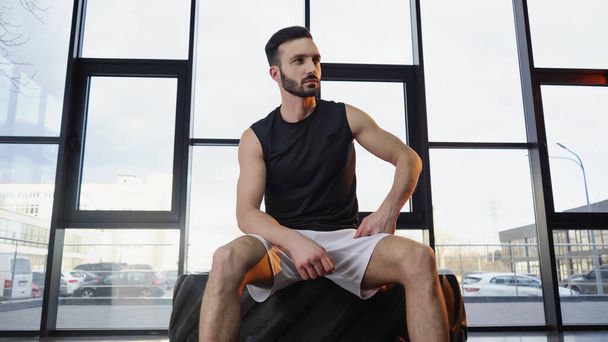 Bearded sportsman sitting on tire in gym  - 写真・画像