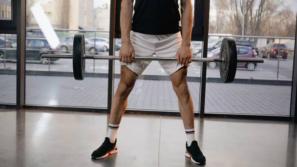 Cropped view of athletic sportsman holding barbell in sports center  - Fotografie, Obrázek