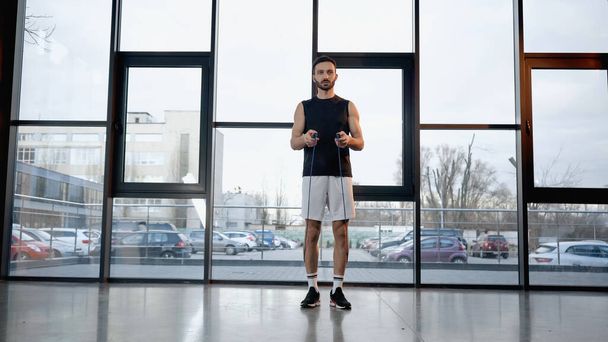 Brunette sportsman holding jump rope in gym  - 写真・画像