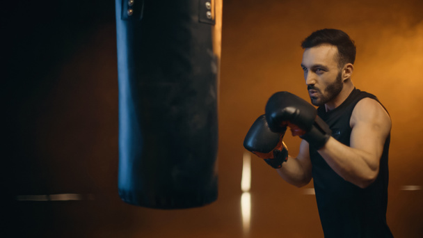 Athletic boxer training with punch bag on dark background - Photo, image