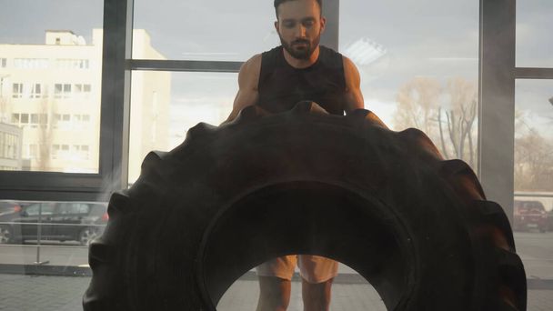 Sportsman lifting tire while training in gym  - Foto, afbeelding