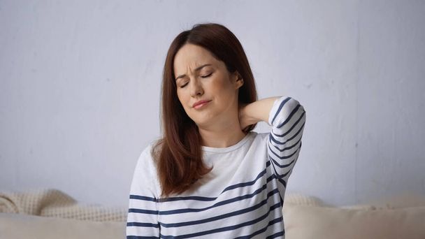женщина с закрытыми глазами, хмурящаяся, чувствуя боль в шее - Фото, изображение