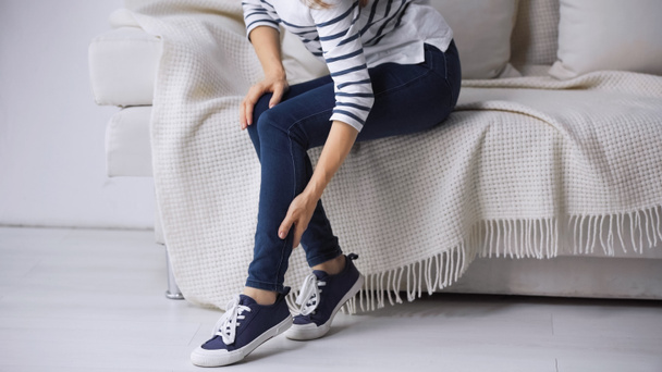 visão parcial da mulher sentada no sofá e tocando a perna dolorosa - Foto, Imagem