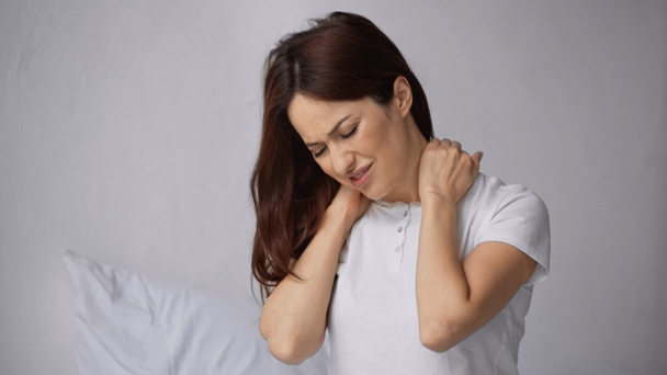 displeased woman frowning while touching painful neck in bedroom - Foto, Imagem