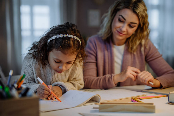 Little girl doing homework with her mother in evening at home. - Fotografie, Obrázek