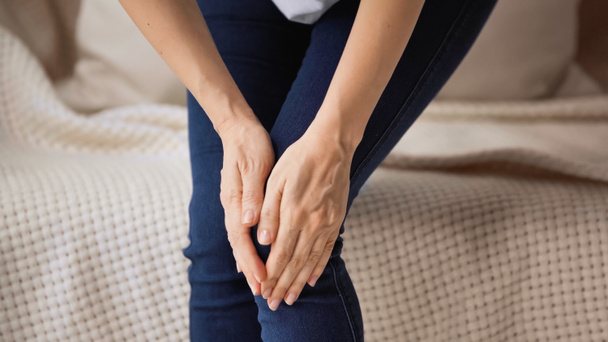 обрізаний вид жінки торкається болючого коліна, стоячи вдома
 - Фото, зображення