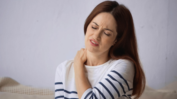 brunette vrouw fronsen met gesloten ogen terwijl het lijden van de nek pijn - Foto, afbeelding