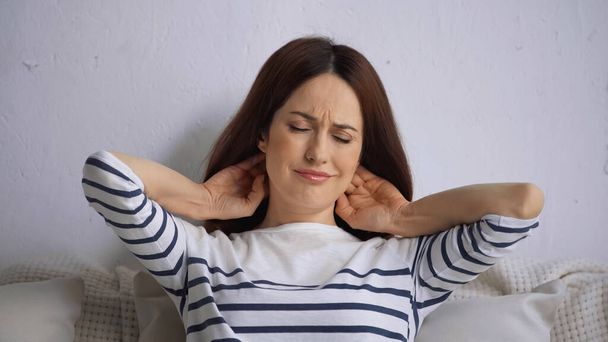 brunette woman with closed eyes frowning while feeling pain in neck - Foto, afbeelding