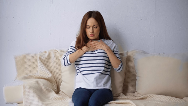 woman with closed eyes sitting on couch and feeling pain in chest - Photo, Image