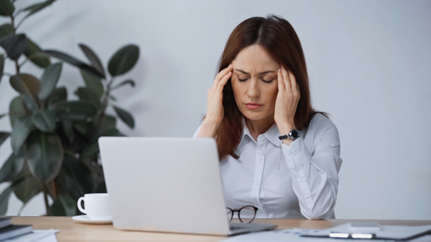 businesswoman with closed eyes touching head while suffering from migraine at workplace - Photo, image