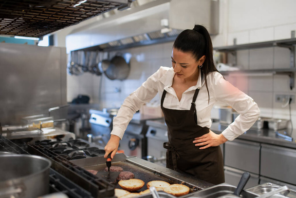 Professional female chef preparing meal indoors in restaurant kitchen. - Фото, изображение
