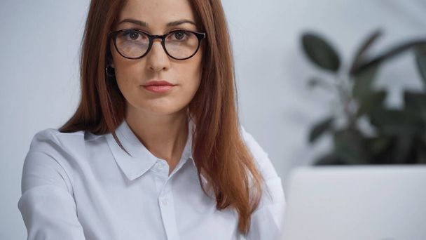 brunetka bizneswoman w okulary patrząc w aparat podczas pracy w biurze - Zdjęcie, obraz