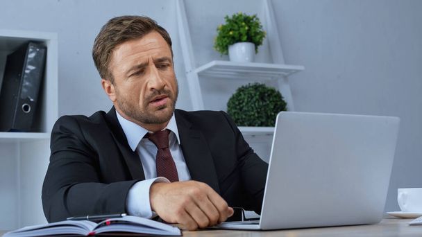pensativo hombre de negocios mirando a la computadora portátil mientras trabaja en la oficina - Foto, Imagen
