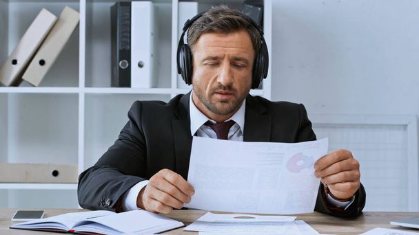 businessman in headphones working with documents near smartphone and notebook on desk - 写真・画像