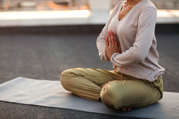 Foto recortada de una mujer irreconocible sentada en una pose de loto sobre una esterilla y practicando yoga, una mujer haciendo un gesto namaste mientras medita al aire libre. Concepto de meditación y atención plena - Foto, imagen