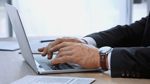 cropped view of businessman in wristwatch typing on laptop in office - 写真・画像