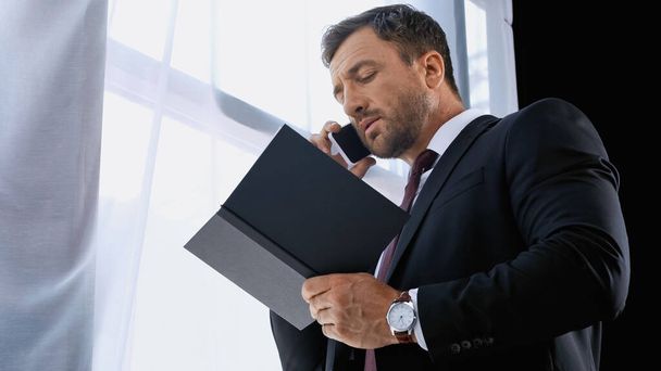 niski kąt widzenia biznesmena z notebooka rozmowy przez telefon komórkowy w biurze - Zdjęcie, obraz