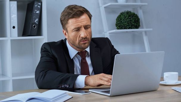 businessman typing on laptop near smartphone and notebook on desk - Fotoğraf, Görsel