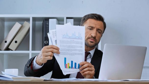 бизнесмен с документами с графиками во время видеозвонка на ноутбуке - Фото, изображение