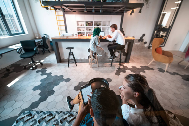 Group of casual multiethnic businesspeople taking a break from the work doing different things while enjoying free time in relaxation area at modern open plan startup office. High-quality photo - Foto, Imagem