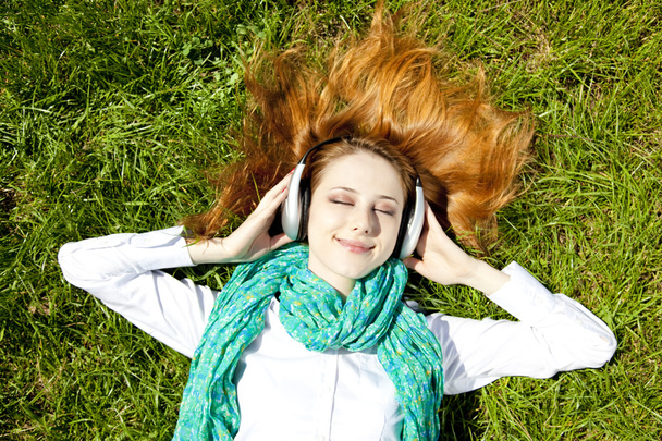 Redhead girl with headphone lies in the park. - Foto, imagen