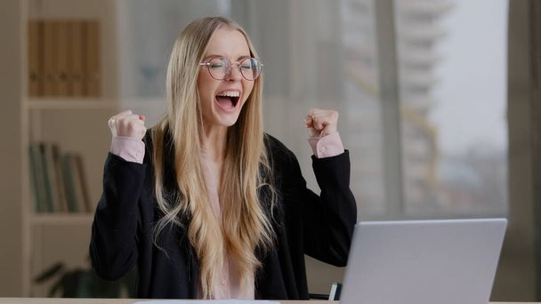 Successful caucasian millennial business woman girl in glasses wins in online betting receives notification with good news positive results offer victory shouts happiness rejoices hands up success - Фото, зображення