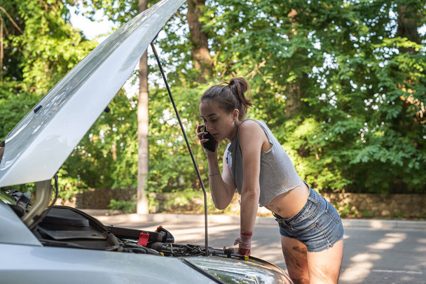 Beautiful young woman open hood and fixing the car on the roadside.  broken-down auto - Fotó, kép