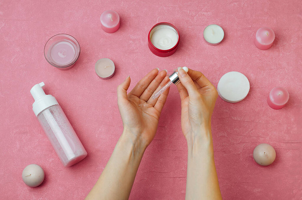 The girl takes care of her hands, pours the serum on her hands to moisturize the skin. Care for nails and cuticles.Female hands top view.Beauty products in the background. - Photo, Image