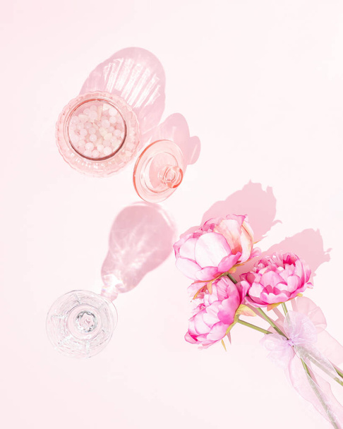 Milujeme kreativní koncept ze skleněné sklenice s růžovými skleněnými perlemi, vinným pohárem a květinami na světle pastelově růžovém pozadí. Plochá umělecká estetika. - Fotografie, Obrázek