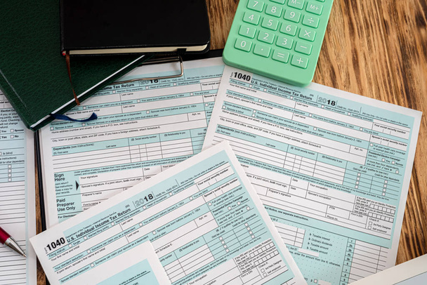 nouvelles formes d'impôt 1040 Etats-Unis avec une calculatrice verte avec un stylo rouge dispersé sur une table en bois. Concept de documentation - Photo, image