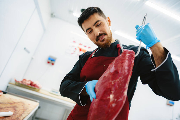 Slachter met vlees aan de haak om het te snijden en te verkopen - Foto, afbeelding