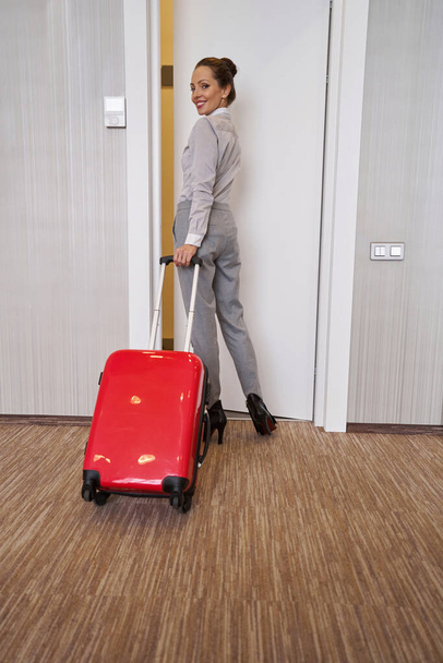 Χαρούμενη γυναίκα με αποσκευές που αφήνει το δωμάτιο του ξενοδοχείου - Φωτογραφία, εικόνα