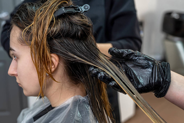 красивая молодая брюнетка девушка сидит на процедуре окрашивания волос у лучшего мастера. Концепция окраски волос. - Фото, изображение