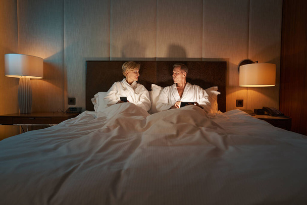 Un par de personas disfrutando de la noche en la acogedora cama del hotel - Foto, imagen