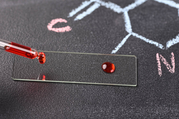 Δύο σταγόνες κόκκινου υγρού στη διαφάνεια μικροσκοπίου και χημικός τύπος στο παρασκήνιο. - Φωτογραφία, εικόνα