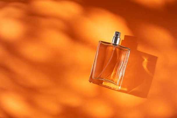 オレンジの背景に透明ボトルの香水。昼との香りのプレゼンテーション。窓の影を持つ天然素材のトレンドコンセプト。女性の本質. - 写真・画像