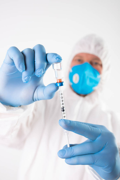 COVID-19 koronavirüs aşısı. Aşı konsepti. Doktorun elinde mavi eldivenler ilaç aşısı şişesi ve şırınga var..  - Fotoğraf, Görsel