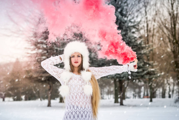 Joven mujer caucásica en suéter con bomba de humo rojo en el día de invierno nieve - Foto, Imagen