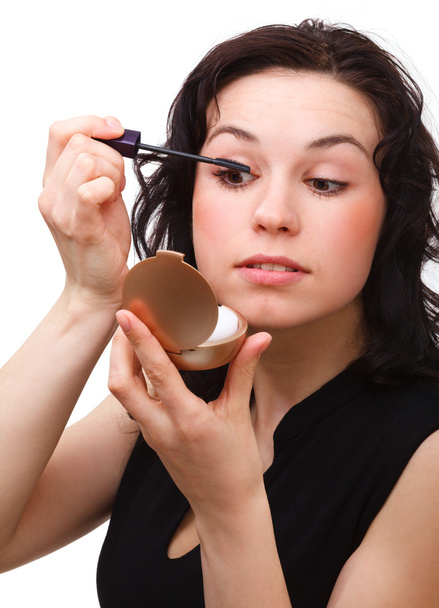 Woman is applying mascara while looking in mirror - Fotoğraf, Görsel