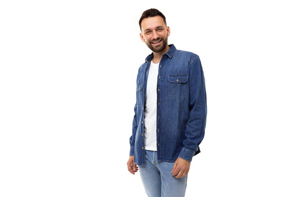young stylish man with a beard in a denim shirt and a white t-shirt looking at the camera on a white background - Fotografie, Obrázek