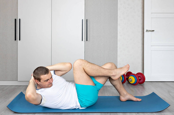 Сильный, здоровый человек с мускулами, тренирующийся дома. Упражнения для мышц прессы. - Фото, изображение