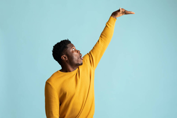 Verbazingwekkende Afro-Amerikaanse man toont hoogte van iets - Foto, afbeelding